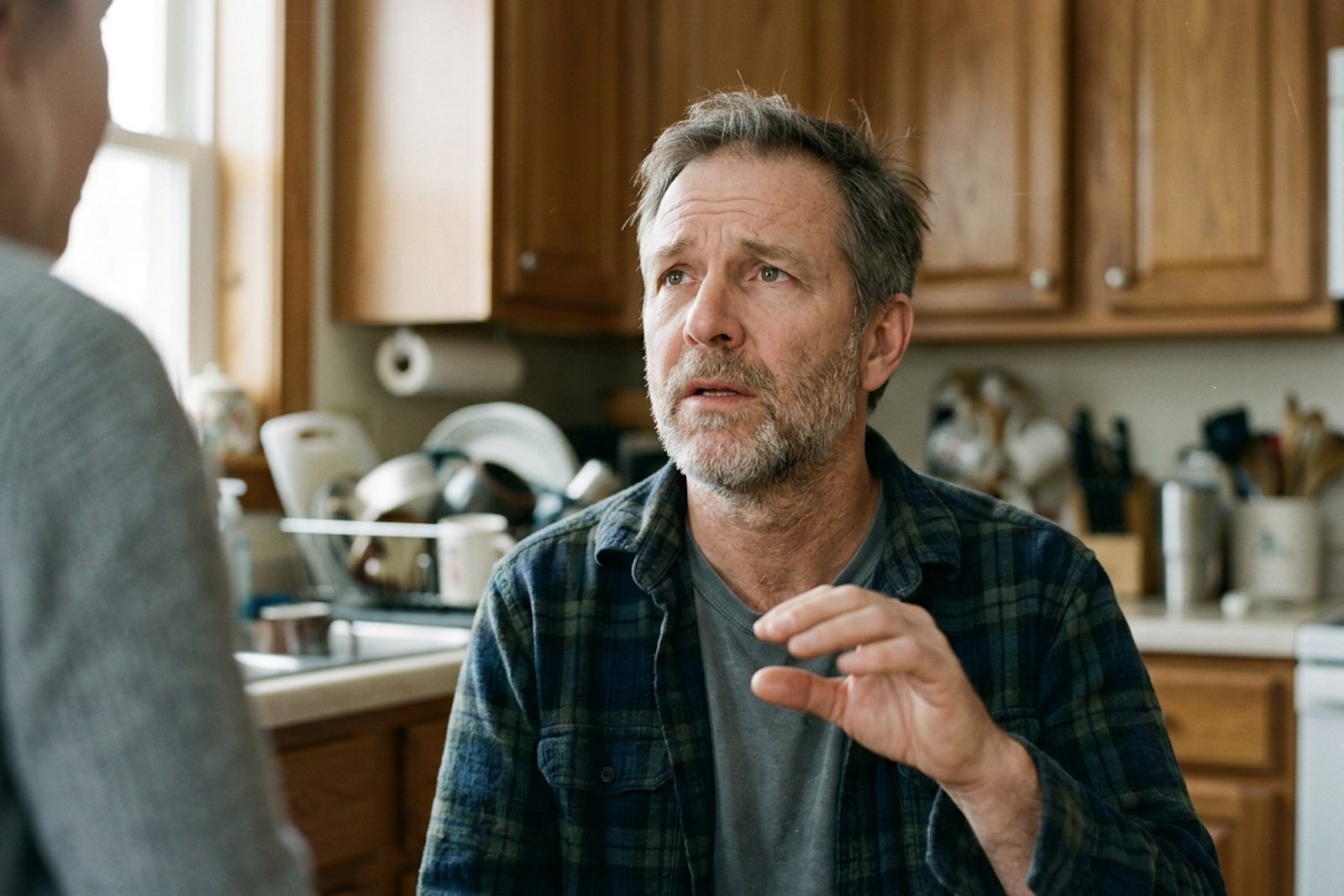 A man in his late fifties pausing mid-conversation in a warm kitchen